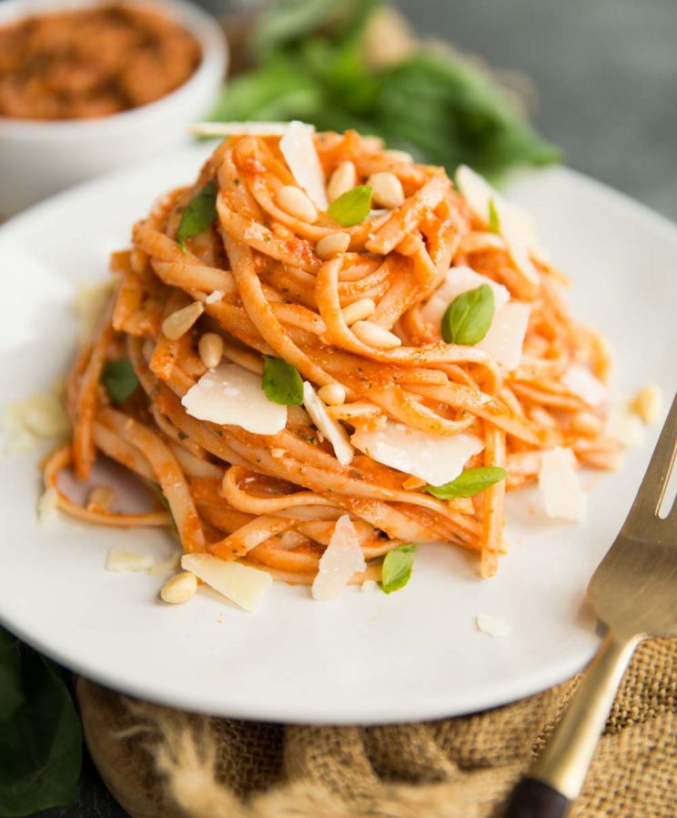 Sun Dried Tomato Pesto Pasta on a white plate with a gold fork and basil in the background