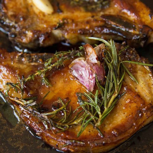 closeup shot of pork chops in skillet garnished with garlic and rosemary