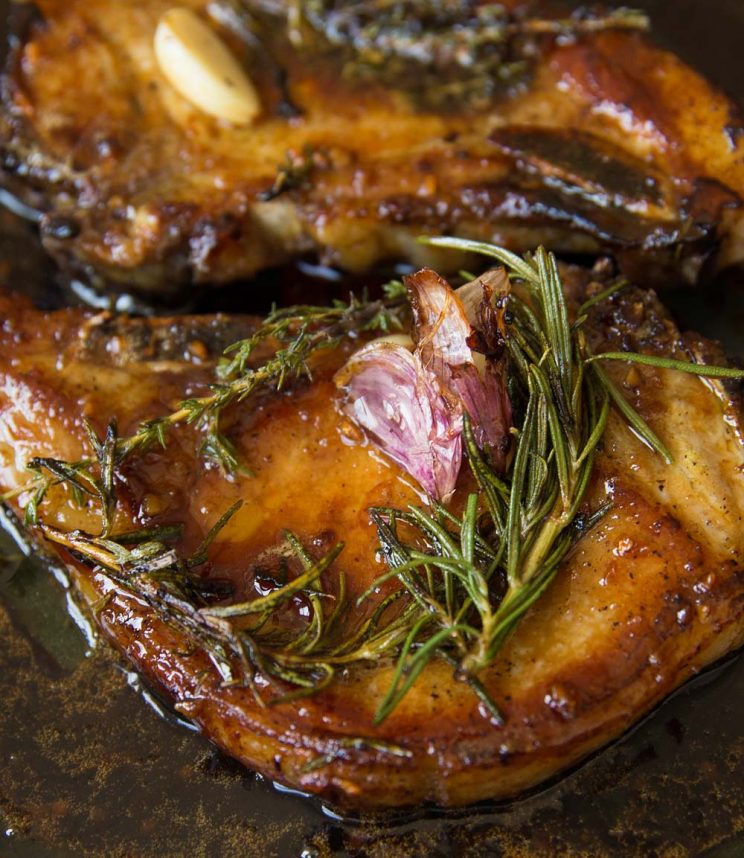 closeup shot of pork chops in skillet garnished with garlic and rosemary