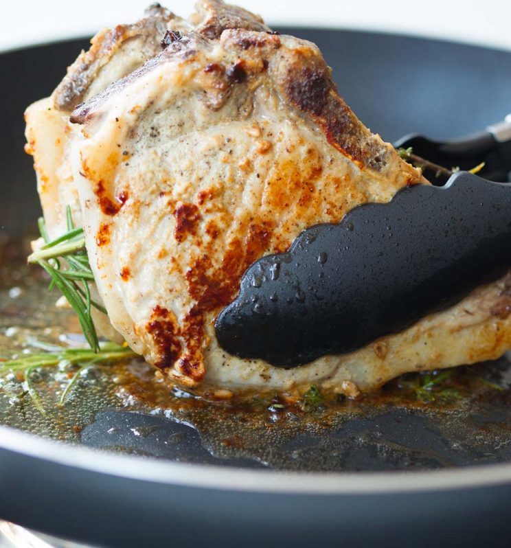 tongs holding pork chops on pan to render fat