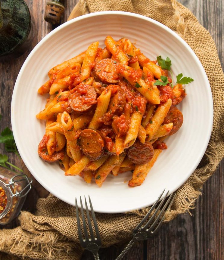 Penne Arrabiata served in a white bowl with two fork on a wooden background
