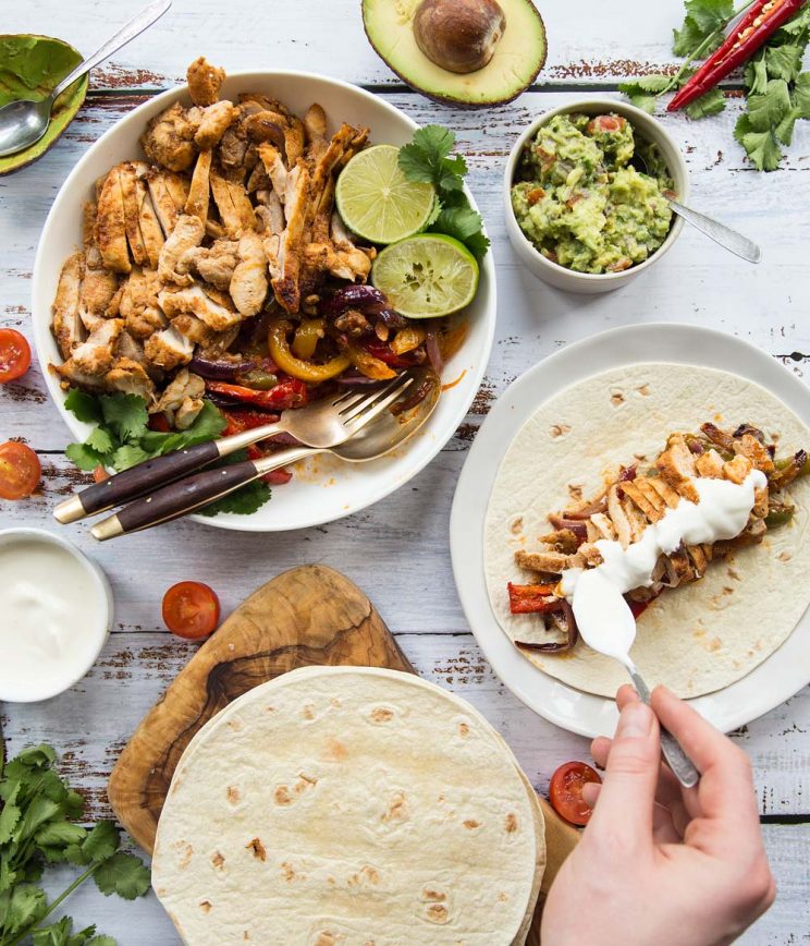 Flat lay of chicken fajitas with sides and garnish including sour cream and guac