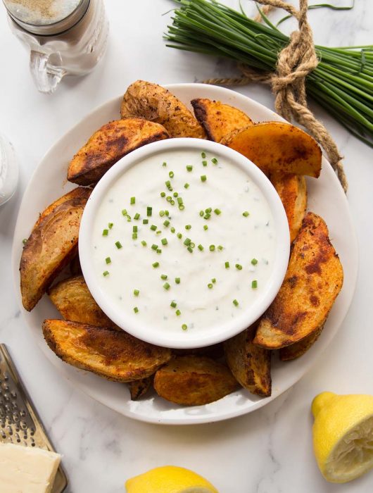 overhead shot of cheese and chive dip on a plate with potato wedges surrounded by garnish