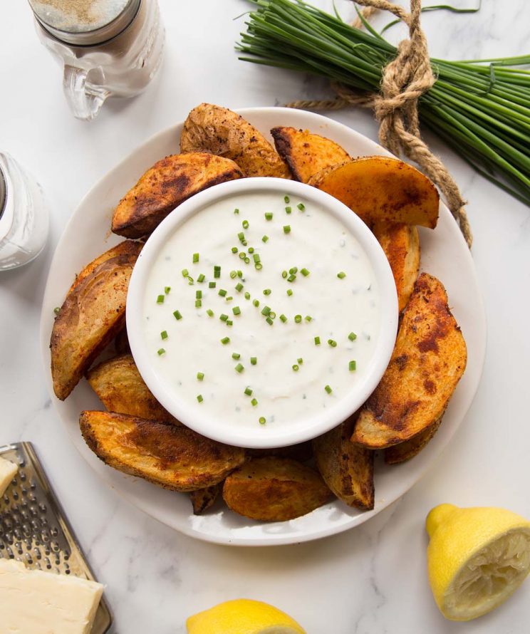 overhead shot of cheese and chive dip on a plate with potato wedges surrounded by garnish