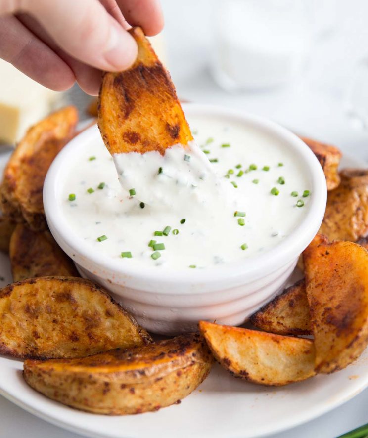 potato wedge being dipped into a cheese and chive dip with wedges circled round the plate