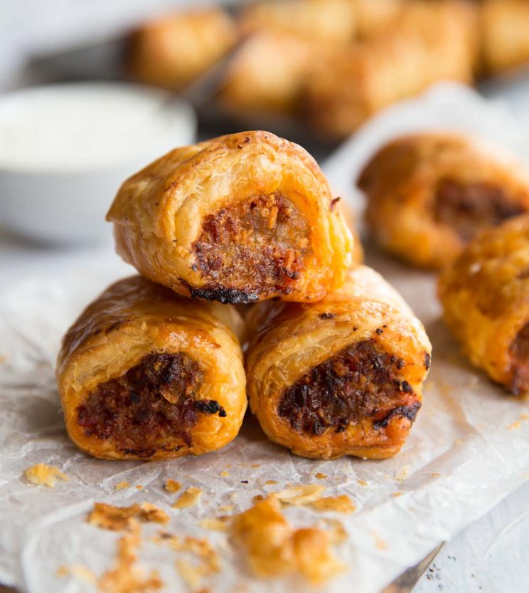 3 Chorizo Sausage Rolls stacked on top of each other with dip and other sausage rolls in the background