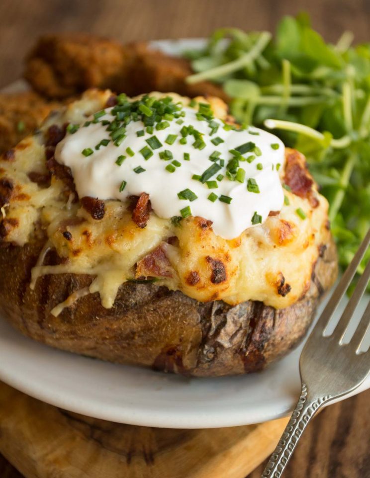 Loaded Potatoes garnished with sour cream and chives with chicken tenders and salad in the background