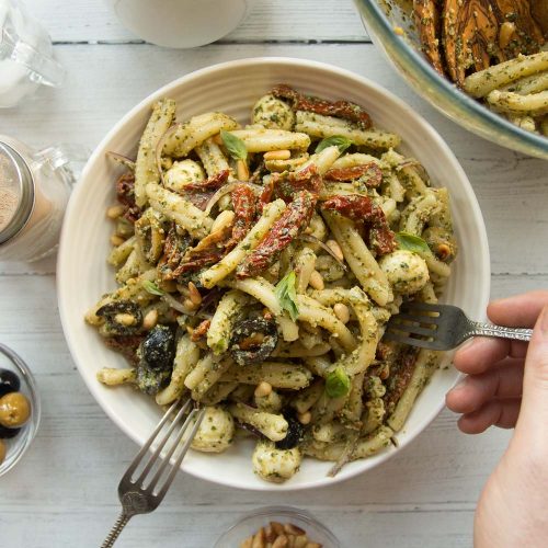 overhead shot of pesto pasta in a white bowl with a hand and fork diving in