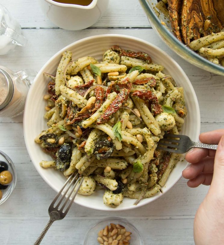 overhead shot of pesto pasta in a white bowl with a hand and fork diving in