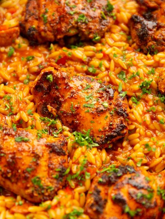 close up shot of spanish chicken orzo in pan garnished with parsley