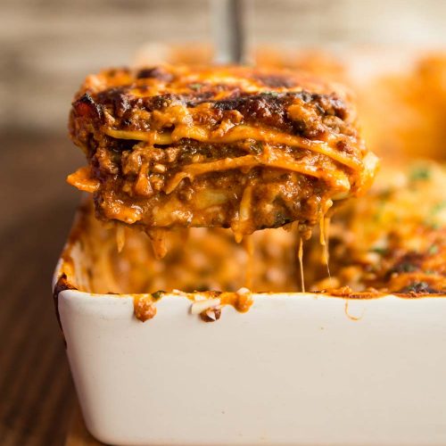 one serving of lasagne being lifted from the baking cheese with cheese hanging off