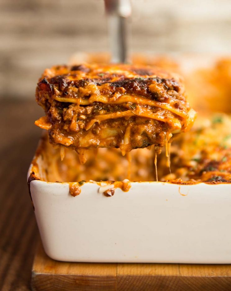 one serving of lasagne being lifted from the baking dish with cheese hanging off