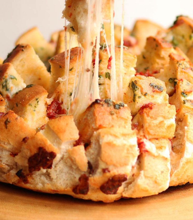 finger pulling section of cheesy bread out of pull apart bread with cheese pull