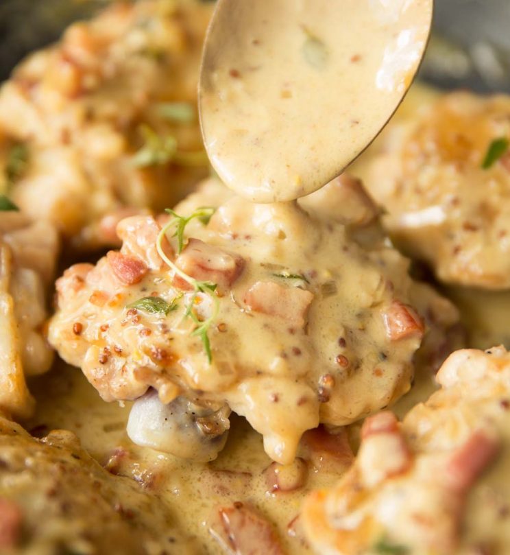 golden spoon pouring sauce over chicken thigh in a skillet