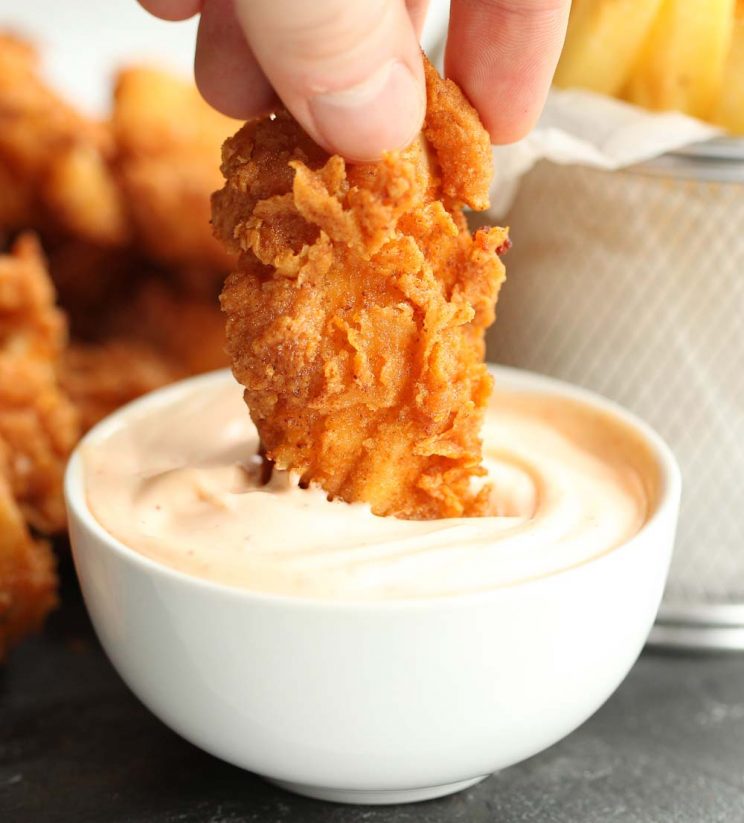 dunking a chicken tender into sriracha mayo in a white bowl.