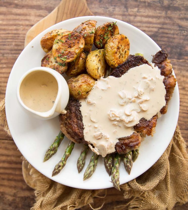 overhead shot of steak with creamy mushroom on top served with asparagus and roasted baby potatoes