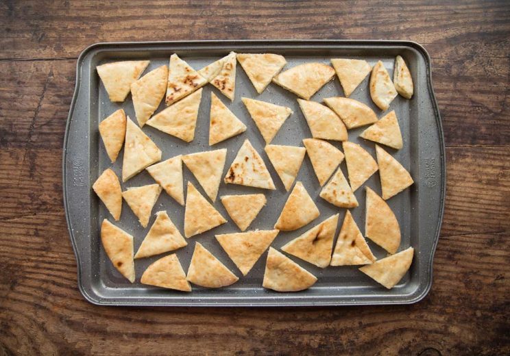 overhead shot of pita chips spread out on oven tray ready to bake