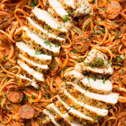 overhead shot of chorizo pasta and sliced grilled chicken on top in pan