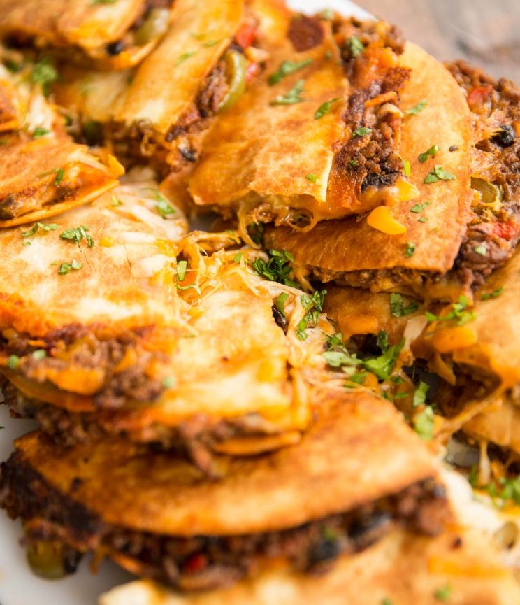 row of quesadillas lined up on a chopping board, sliced in half with cheese pouring out