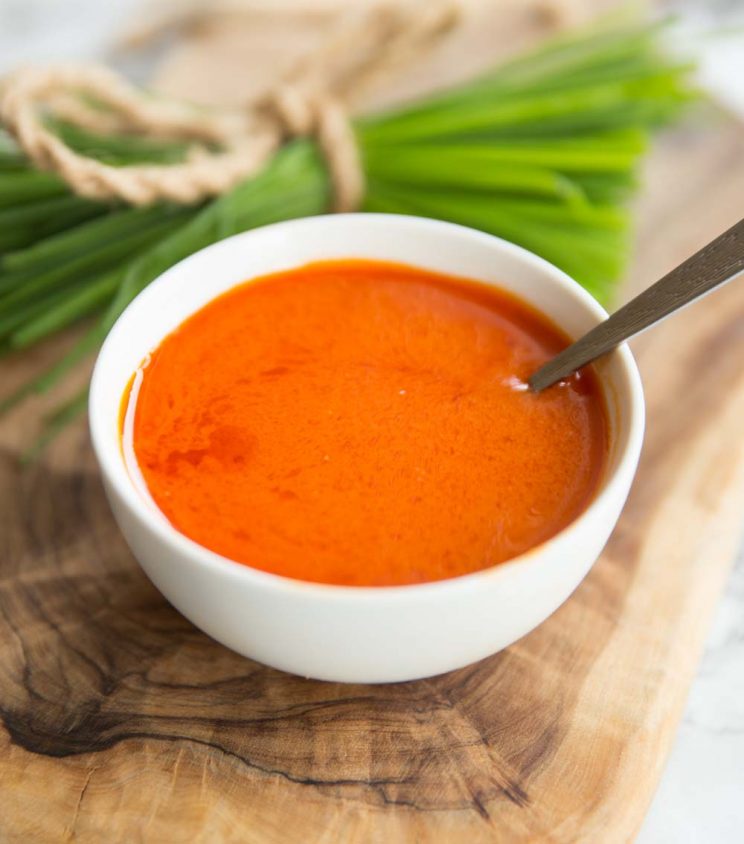 buffalo sauce in a small white pot with spoon in it and chives blurred in the background