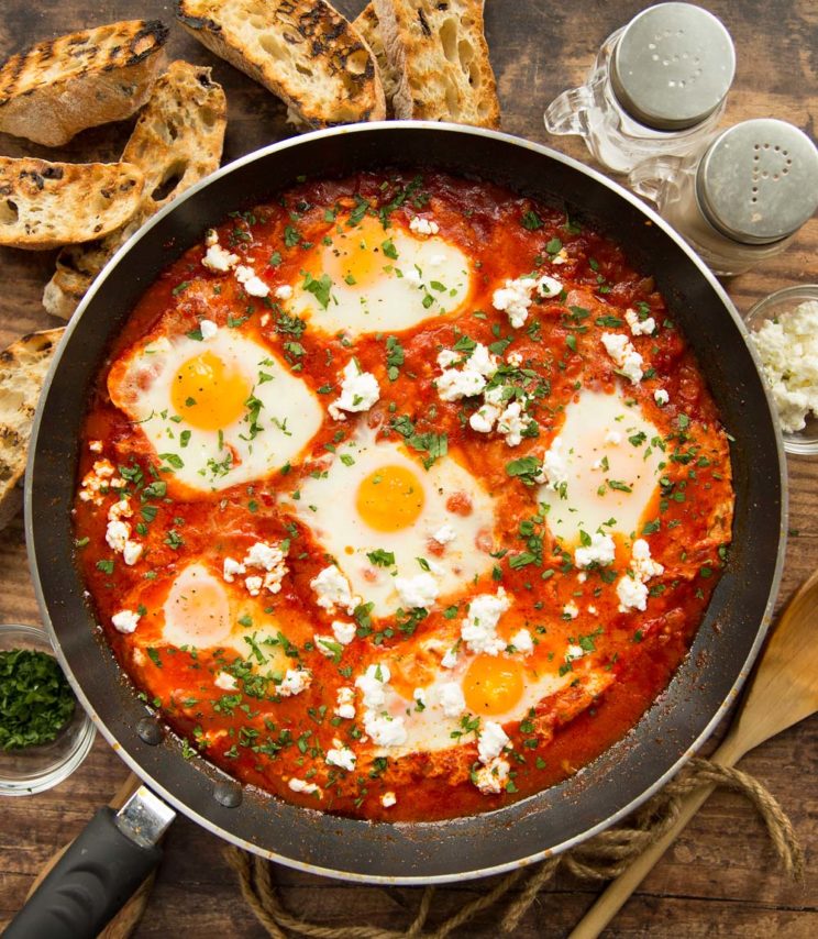 overhead shot of shakshuka in pan surrounded by ciabatta and seasonings