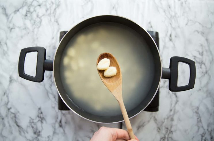 gnocchi in a pot of boiling water, lifting up two pieces on a wooden spoon