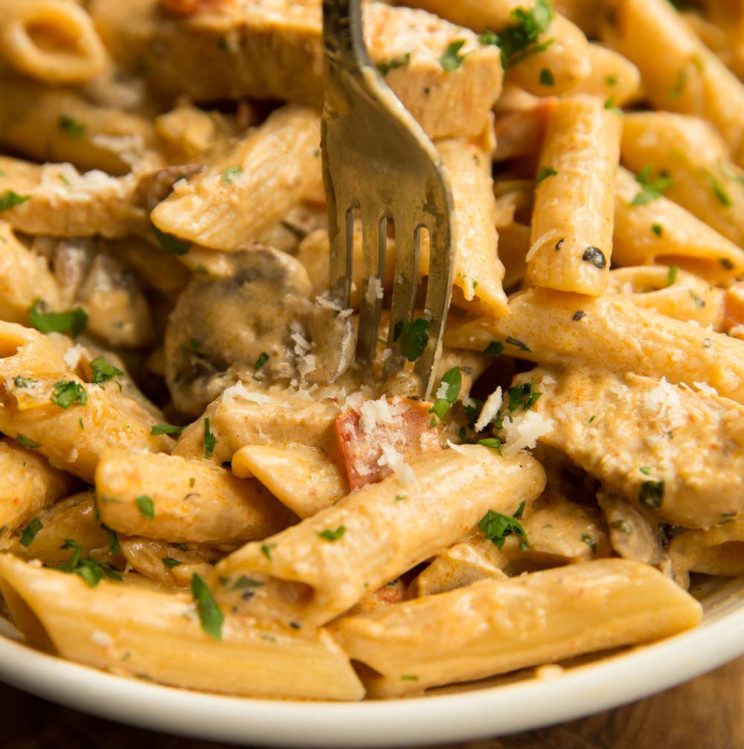 cajun chicken pasta served in white bowl with fork digging in