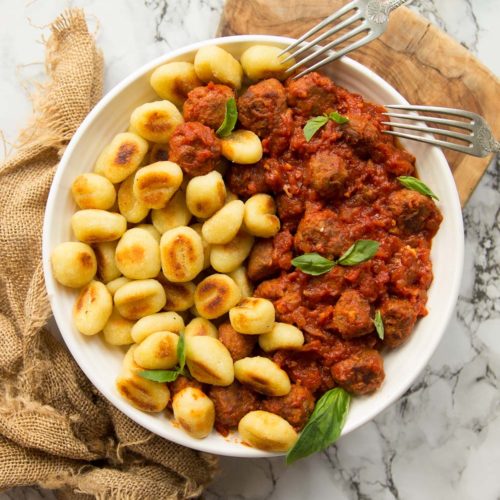 overhead shot of gnocchi and sausage meatballs in white bowl on brown chopping board