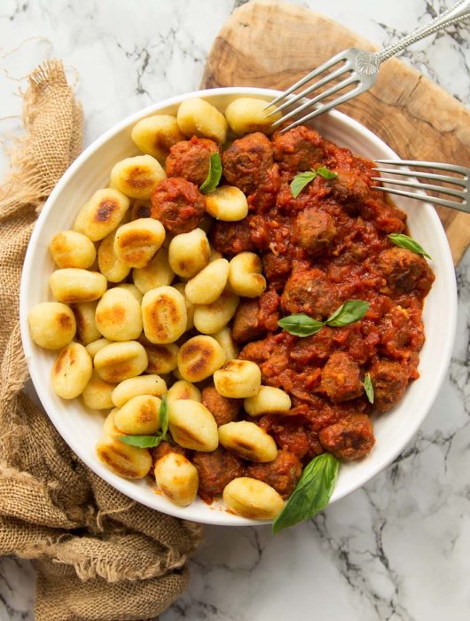 overhead shot of gnocchi and sausage meatballs in white bowl on brown chopping board