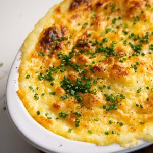 close up shot of cheese and garlic mashed potatoes served in white baking dish with fresh chives