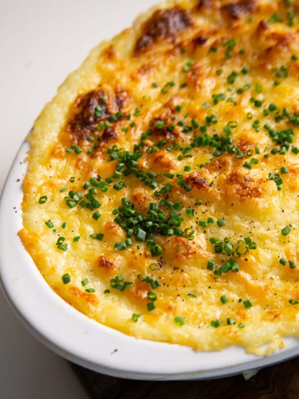 close up shot of cheese and garlic mashed potatoes served in white baking dish with fresh chives