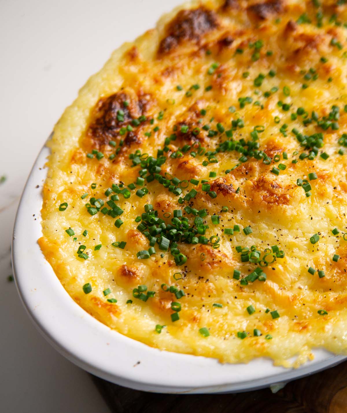 close up shot of cheese and garlic mashed potatoes served in white baking dish with fresh chives