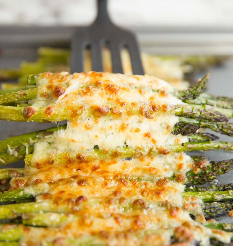 cheesy asparagus on baking tray with spatula ready to pull up from underneath
