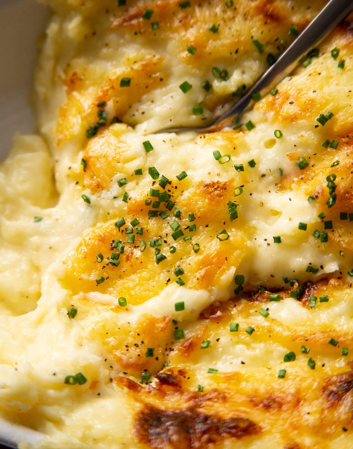 close up shot of spoon digging into bowl of cheesy garlic mash