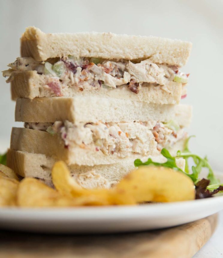 3 half sandwiches stacked on a white plate with crisps and salad leaves