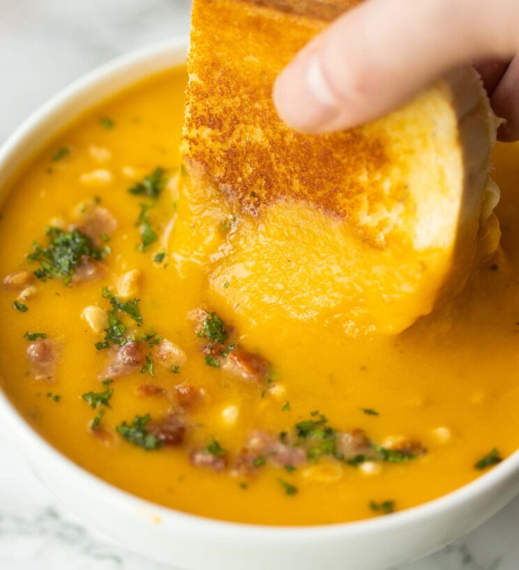 close up shot of hand dunkng grilled cheese into butternut squash soup