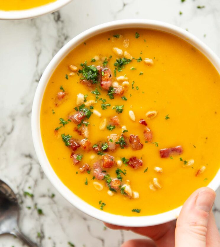 overhead shot of butternut squash soup in white bowl with toppings on marble backdrop