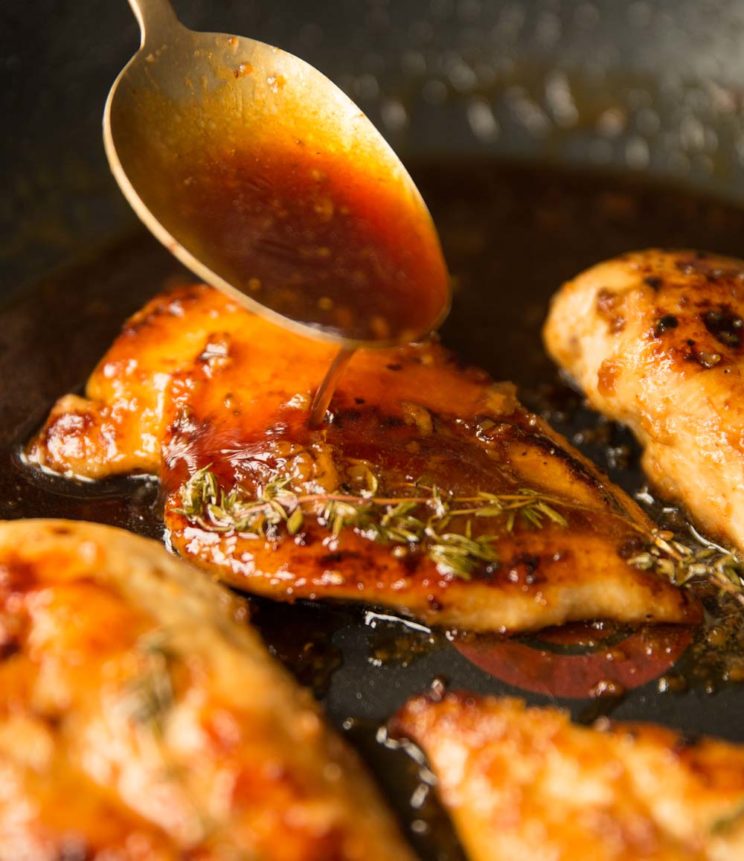 pouring honey garlic sauce on chicken breast in skillet with golden spoon