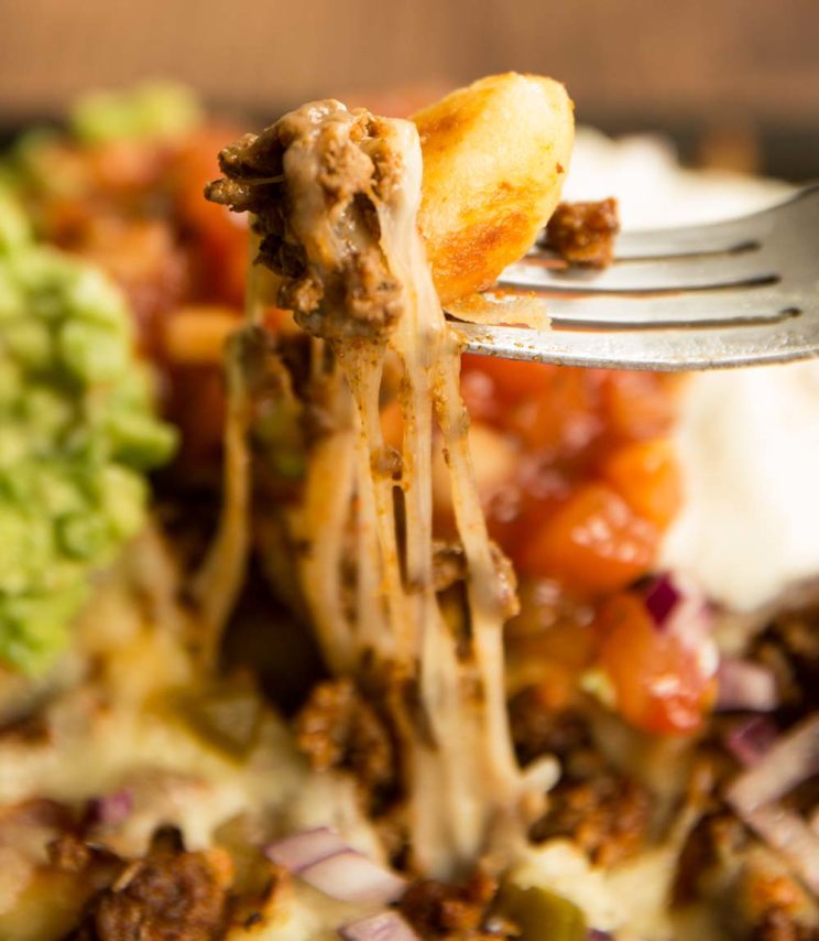 fork pulling gnocchi out of nachos tray with cheese pulling away