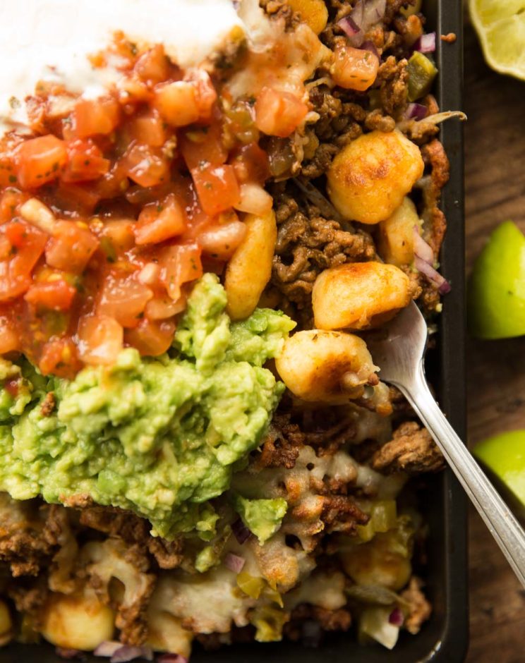 overhead shot of gnocchi nachos in tray with guac, salsa ad sour cream