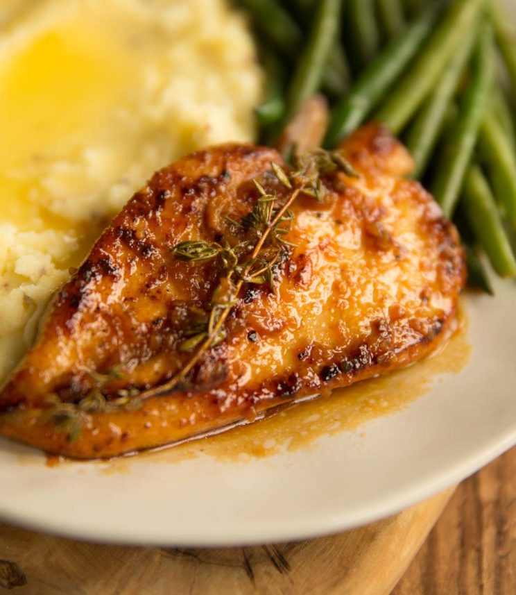 honey garlic chicken breast on plate with mashed potatoes and green beans blurred in the background