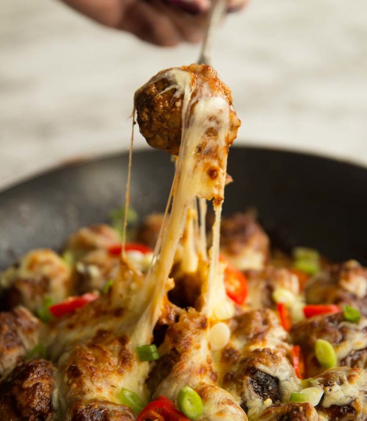 pulling meatball out of skillet with fork and cheese dripping down