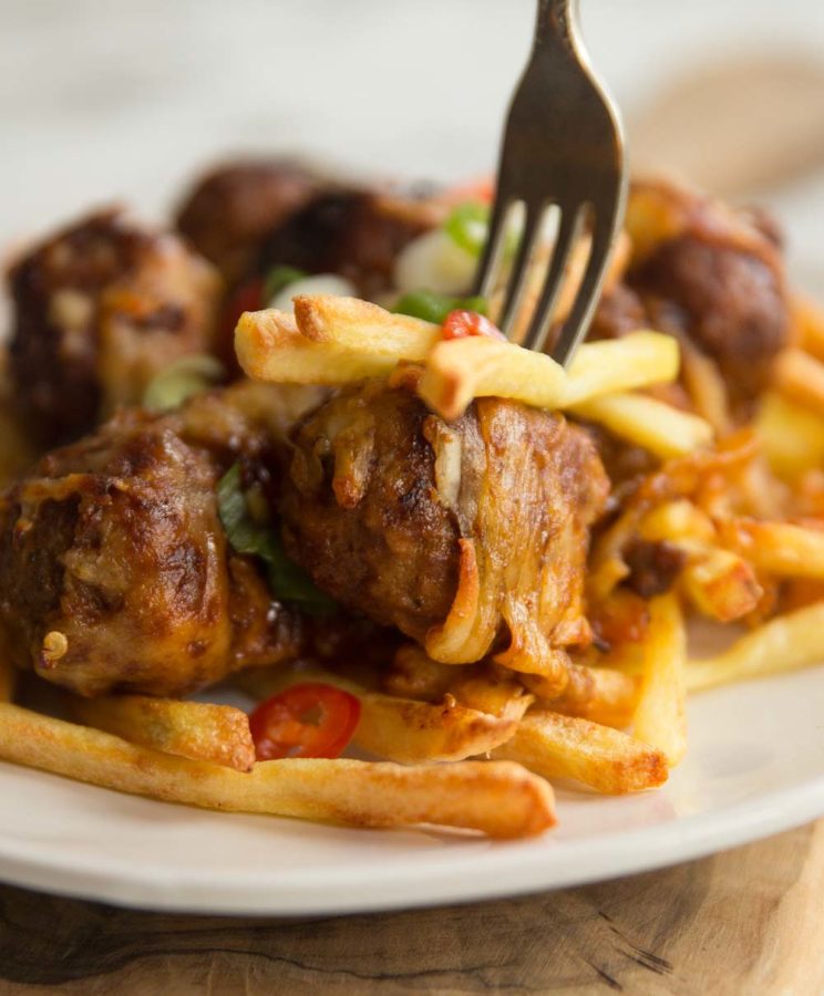 closeup of stabbing fork into meatball and fries