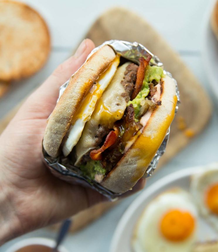 holding breakfast burger to camera with ingredients blurred in background