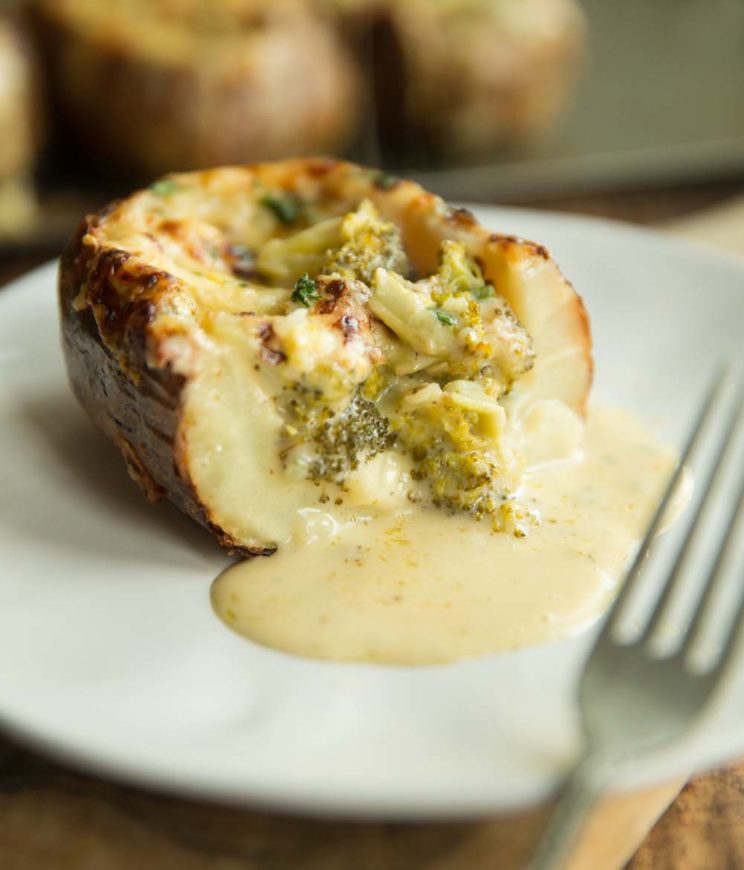 cheesy broccoli spilling out of potato on white plate