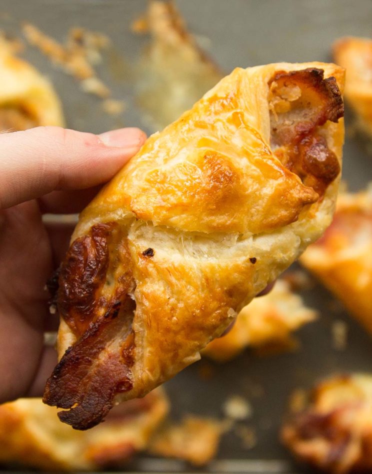 holding cheese and bacon wrap pastry to camera with more blurred underneath