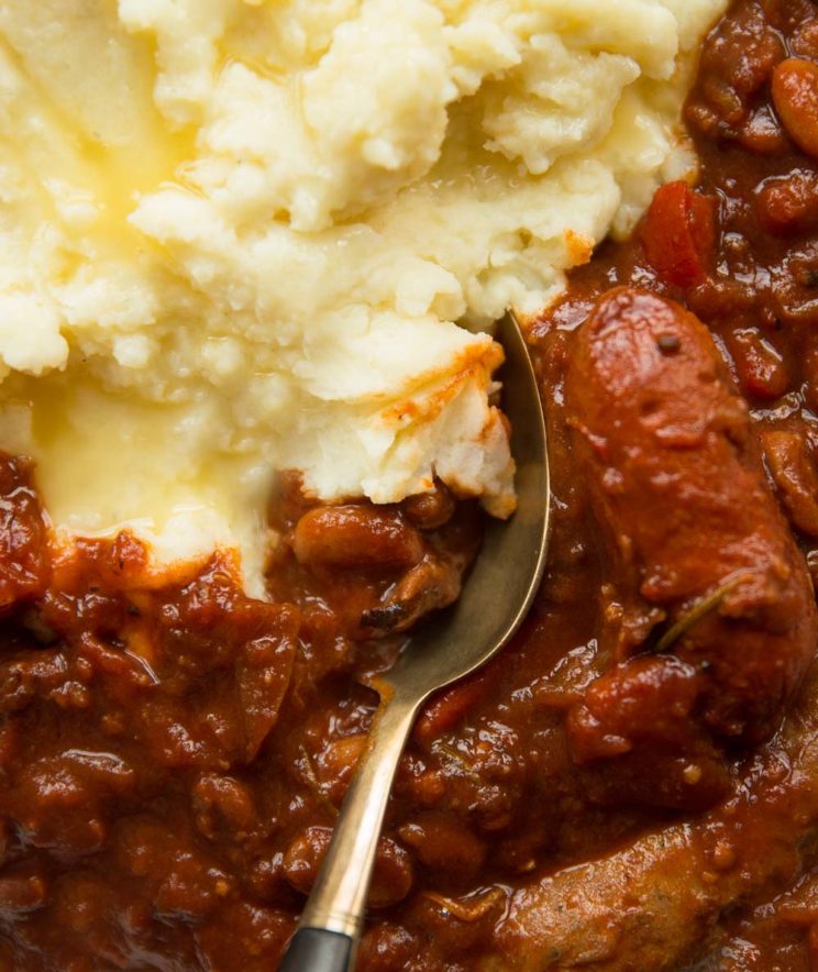 overhead shot of sausage and bean casserole with mashed potato and spoon digging in