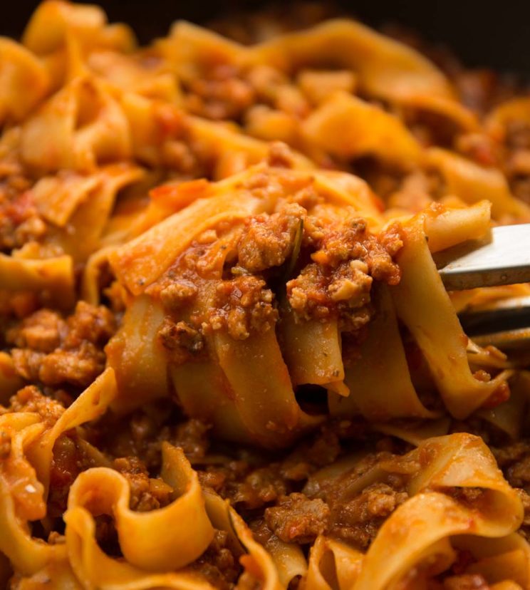 pasta tongs twirling sausage ragu in pan