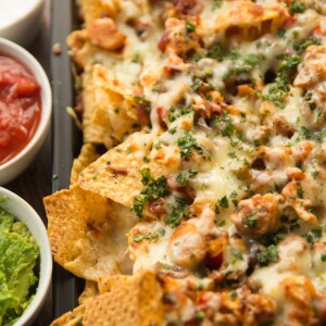 chicken fajita nachos garnished with coriander served on a tray with dips next to them