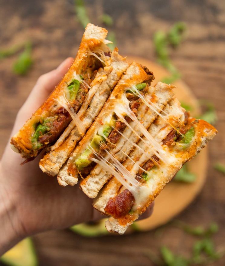 holding chorizo grilled cheese to camera showing filling with ingredients blurred behind